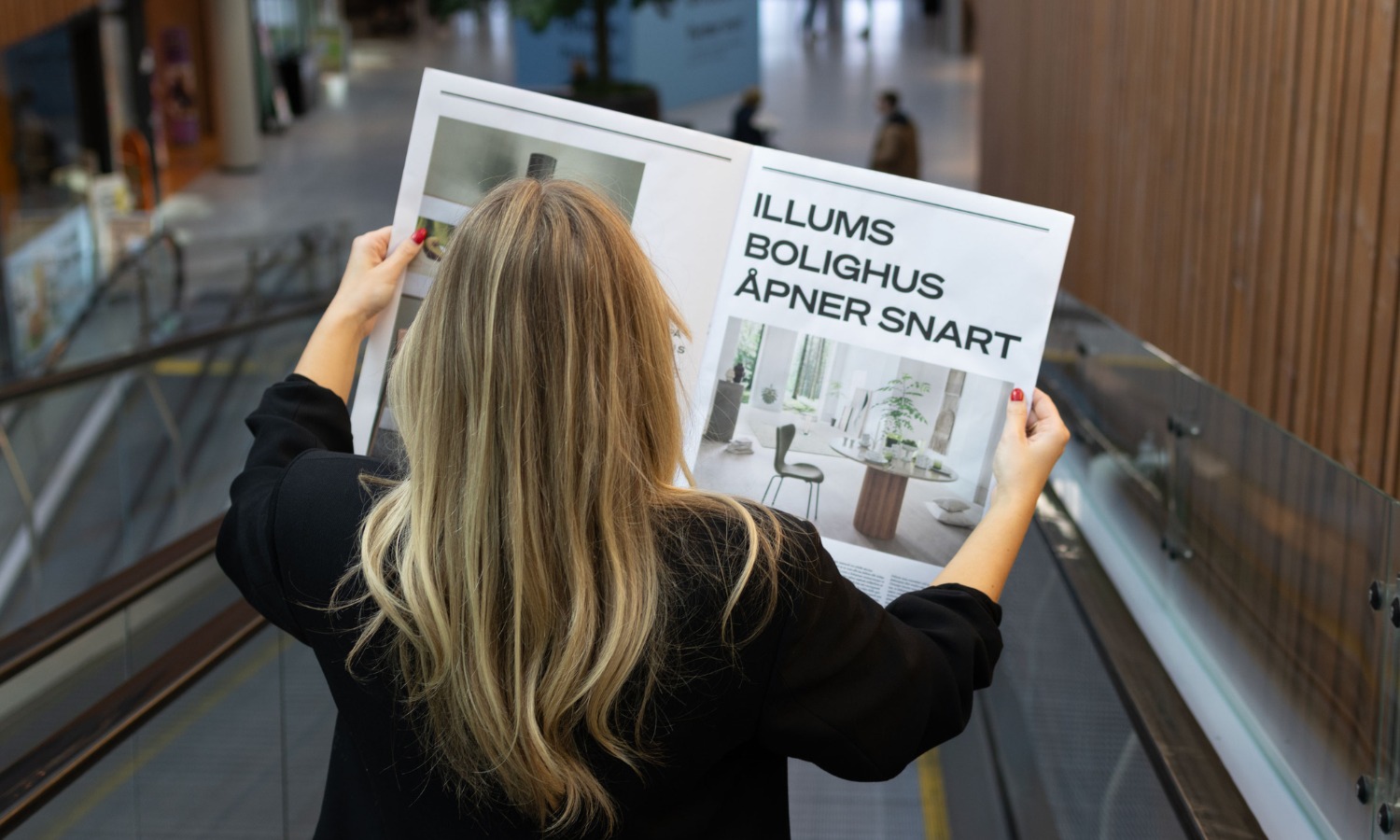 Bildet av en jente som holder en avis i rulletrappen, hvor det står at Illums Bolighus åpner snart.